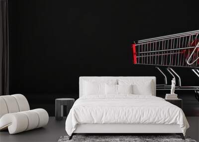 Empty shopping cart with red accents, placed against a dark, minimalist background. The reflective metal contrasts with the black backdrop, emphasizing the cart's sleek design Wall mural