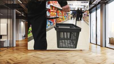 A man with a basket walks in a supermarket. Hand and part of the basket in focus, blurred background Wall mural