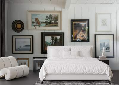 A white wall features a curated collection of framed landscape paintings, showcasing various scenery and perspectives Wall mural