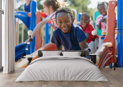 African american young boy smiles as he sits on a playground slide with other children playing around him Wall mural