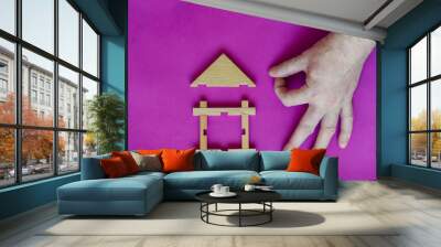 Male hand shares click with sticks on the roof of toy children wooden house on lilac background. Wall mural