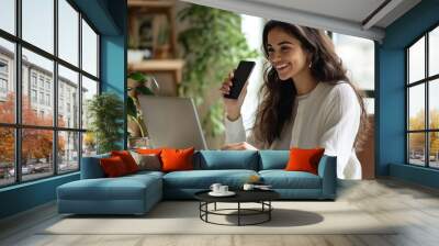 Smiling female entrepreneur engaging in productive work on laptop while talking on smartphone Wall mural