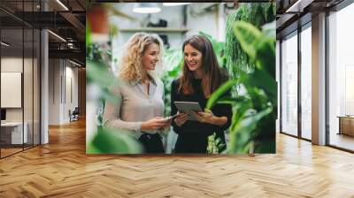 Smiling young and middle aged businesswomen discussing with digital tablet in green office Wall mural