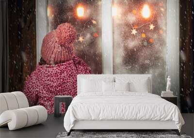 On Christmas night an adorable little girl near the window the snow falls. Wall mural