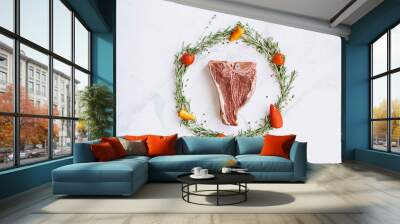 raw t-bone steak in the center of a Christmas wreath of rosemary thyme cherry tomatoes and bell peppers on a white marble surface. christmas dinner concept Wall mural