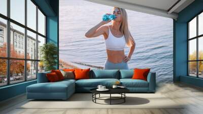 woman in tracksuit by the sea drinks water after workout Wall mural