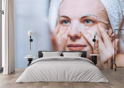 woman stands near a mirror with a towel on her head and puts on a cosmetic mask Wall mural