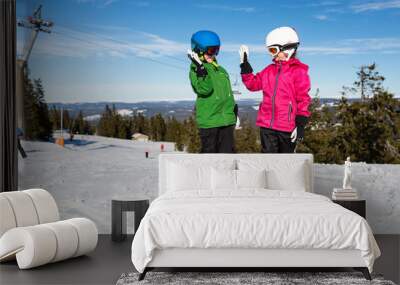 Two child skiers doing a high five at ski slope Wall mural