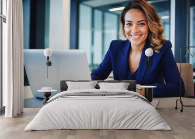 A businesswoman smiles while working on her laptop at her desk in a modern office Wall mural