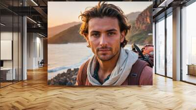 A young man with a backpack stands on a beach, overlooking the ocean at sunset Wall mural