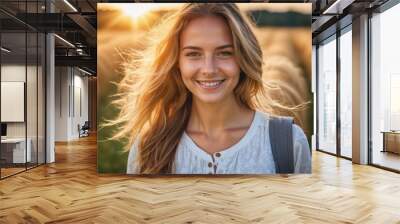 A young woman smiles brightly in a field of tall grass, the sun setting behind her Wall mural