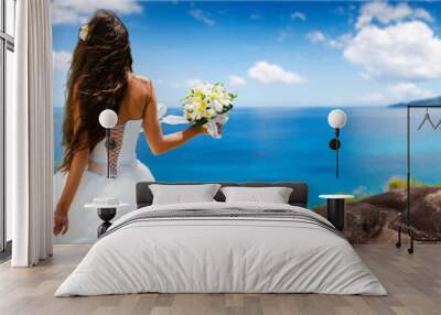 bride, beautiful young girl with dark hair in a white wedding dress with bouquet on  background of beach with blue water. Seychelles Wall mural