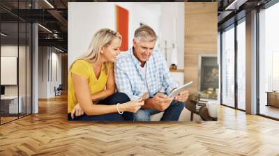 Beautiful, smiling mature couple buying online, shopping on their digital tablet together on their home living room sofa. Husband making financial payments through internet banking with his wife Wall mural