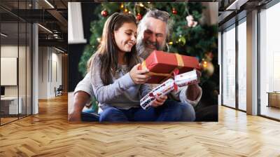 Grandpa, child and gift by Christmas tree in home, festive season and present for bonding on xmas. Grandfather, girl and happy for package on religious holiday, celebration and love for tradition Wall mural