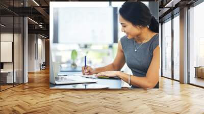 Putting plans into perspective and on paper. Cropped shot of a young businesswoman writing notes while working on a laptop in a modern office. Wall mural