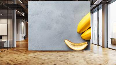  A ripe banana and a cluster of plums on a gray surface One banana is half-peeled Wall mural