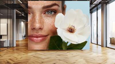  A woman with freckled skin holds a white flower, set against a blue backdrop Wall mural