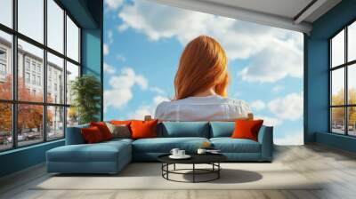  Woman's head in chair facing blue sky with white clouds behind Wall mural