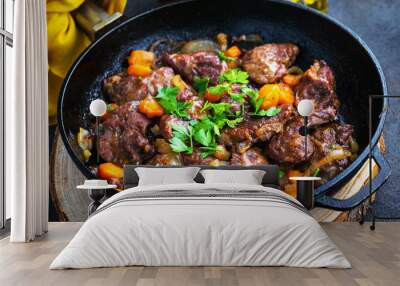 Pork cheeks stewed with vegetables in an iron pan, sliced bread, olive oil, with a dark background in a single shot above. Wall mural