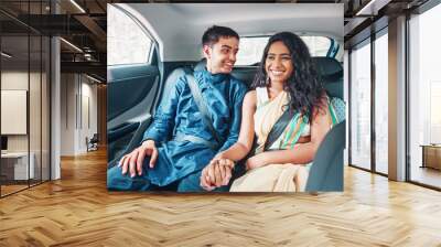 Beautiful Indian couple in ethnic dress traveling on a back seat of a car, holding hands and laughing Wall mural