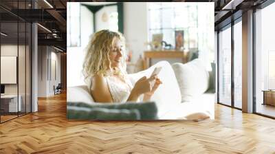 Beautiful woman in light interior relaxing while using her mobile phone Wall mural