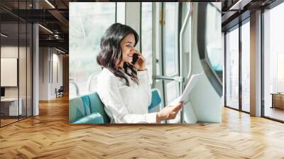 Young Indian businesswoman reading documents and talking on phone in Dubai tram Wall mural