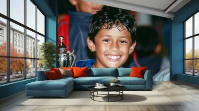 A boy smiling and holding a trophy after winning a soccer match Wall mural