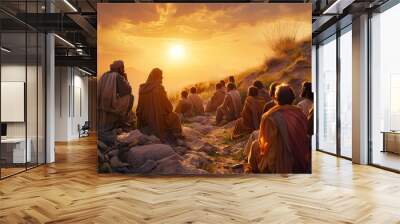 A group of people are sitting on a hillside, watching the sun set Wall mural