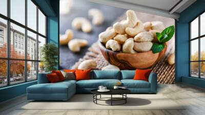 Cashew nuts in wooden bowl on dark black table with mint leaf on top. Raw cashews side view. Wall mural