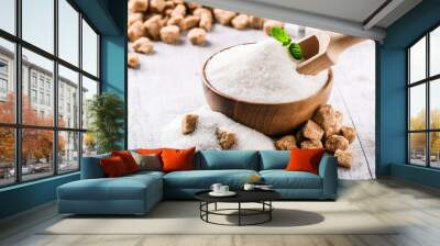 White sugar in wooden bowl with scoop and green mint leaf. Brown cugar cubes on white table. Wall mural