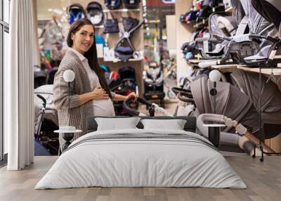 A beautiful pregnant woman is choosing a stroller for her baby in the baby shop  Wall mural