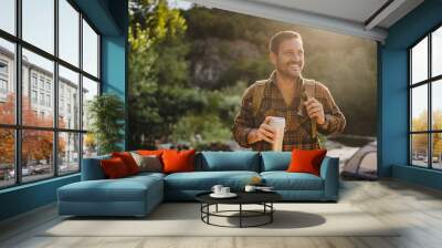 Adult caucasian man hold thermos and drink in front tent near river Wall mural