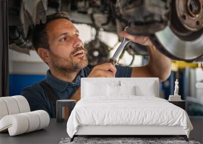 Car mechanic use a wrench to repair automobile undercarriage system Wall mural