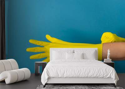 Close up on hand of unknown caucasian woman female girl putting on adjusting holding protective yellow rubber gloves to clean or disinfection against blue wall background in day Wall mural