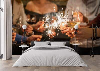 Close up on hands of group of people holding glasses of wine and sparkles while toasting and celebrating indoor focus on glass of wine birthday or new year celebration concept Wall mural