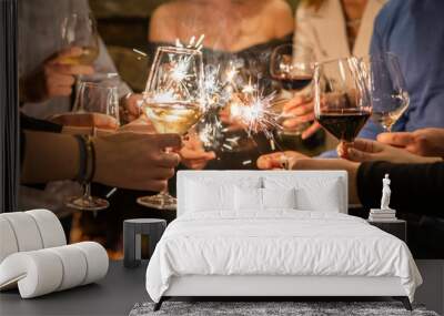 Close up on hands of group of people holding glasses of wine and sparkles while toasting and celebrating indoor focus on sparks birthday or new year celebration concept Wall mural