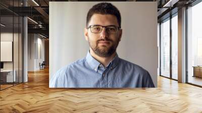 Close up portrait of young caucasian man adult wearing shirt and eyeglasses standing by the window front view short hair and beard Wall mural