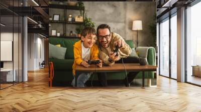 Father and son play video games with joystick and have fun at home Wall mural