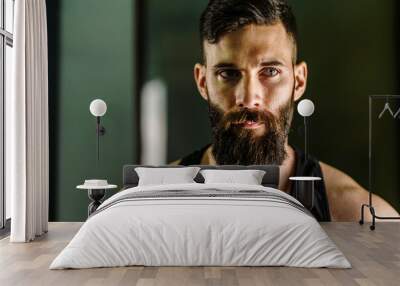 Front view close up portrait of young adult caucasian man with dark hair and beard in black shirt hoodie looking to the camera in dark - Confident modern male dramatic portrait with copy space Wall mural