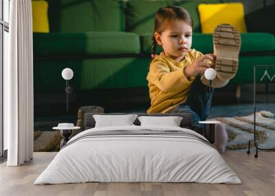 girl toddler child puts on her own boots in the winter at home Wall mural