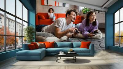 group of people caucasian family man and woman mother and father with child girl lying on the floor at home playing video game console using joystick or controller real people having fun happy smiling Wall mural