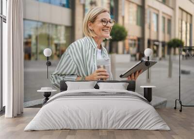 Happy mature woman sit with thermos use digital tablet on the street Wall mural