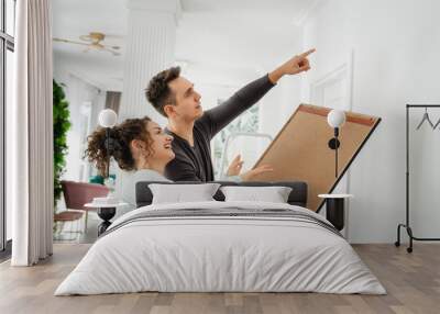 man and woman caucasian couple hanging painting on the wall at home Wall mural