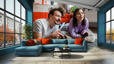 Man and woman lying on the floor at home playing video game console Wall mural