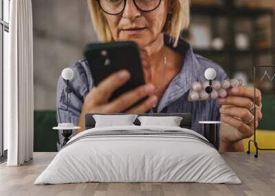 Mature woman hold the medicine and read instructions on mobile phone Wall mural