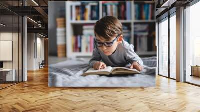 One caucasian boy lying on the floor at home in day reading a book front view wearing eyeglasses copy space real people Wall mural