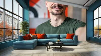 One man young adult caucasian male standing at home with brown hair mustaches and beard looking to the camera happy smile confident real people green t shirt UGC selfie user generated content Wall mural