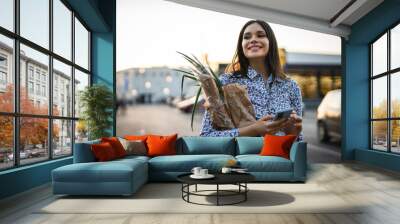 one woman front view waist up portrait of beautiful young adult brunette holding groceries while walking or standing at parking lot in front of the shopping center in evening happy smile copy space Wall mural