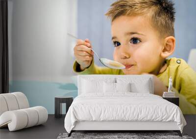 Portrait of small boy child eating soup meal or breakfast having lunch by the table at home with spoon white kindergarten Wall mural