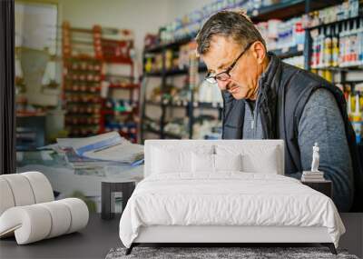 Senior man entrepreneur at his office store by the table accounting check bill calculation receipt making invoice for selling goods salesman at warehouse depot storehouse Wall mural